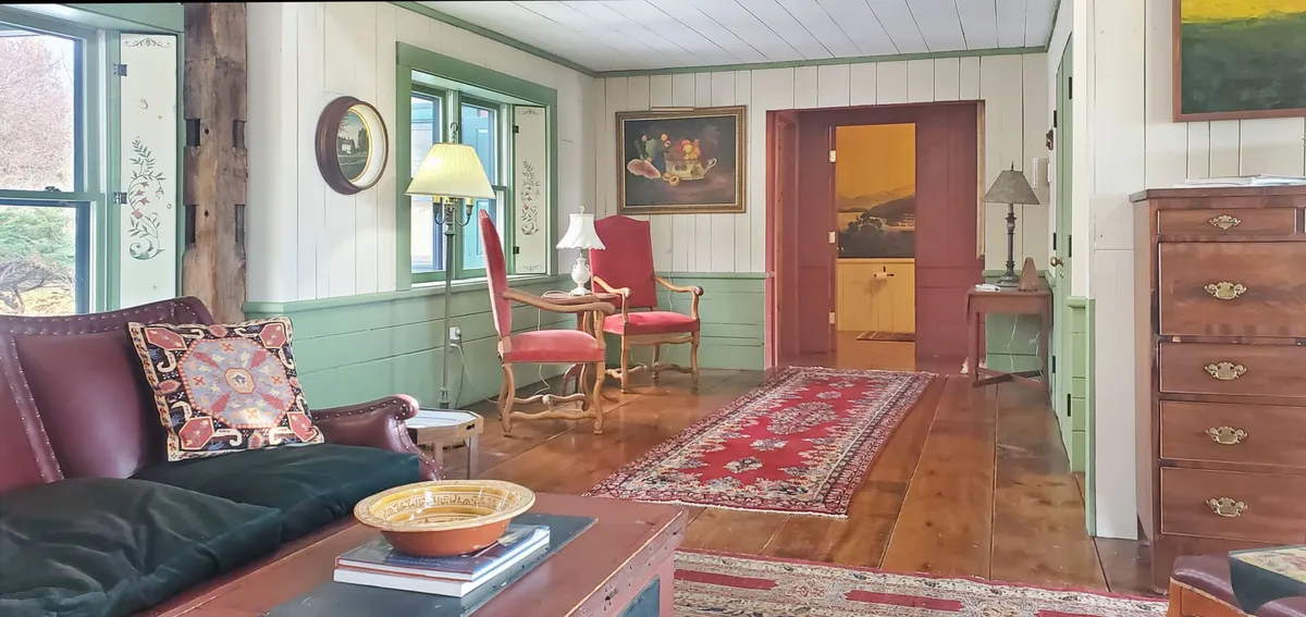 An intimate and inviting corner featuring a leather sofa, a patterned rug, a classic lamp, original paintings, and wooden furniture. The setup suggests a perfect spot for curling up with a good book or engaging in thoughtful conversation amid artistic surroundings.